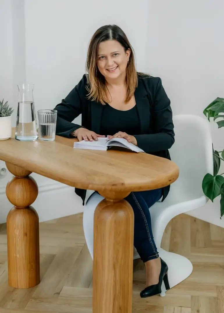 Anna Trzebuniak w ciemnej marynarce siedząca przy stoliku, na którym leży książka